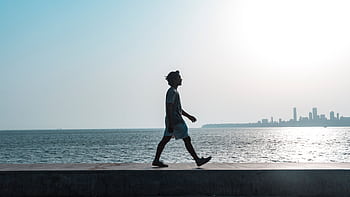 A silhouette of a man walking along the Mumbai coastline at sunset with a cityscape backdrop. HD wallpaper