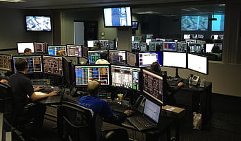 A bustling control room with people working on multiple computer monitors. HD wallpaper
