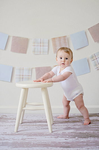 Cute baby standing by a stool indoors with a playful background. HD phone wallpaper