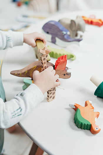A young child creatively plays with colorful wooden toys on a table, fostering imagination and learning. HD phone wallpaper