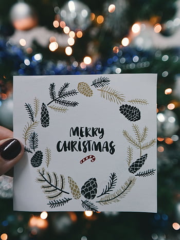Merry Christmas card held in front of decorative tree with bokeh lights. HD phone wallpaper