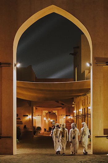 Men in traditional attire walking through illuminated arches at night, showcasing Islamic architecture. HD phone wallpaper