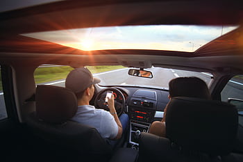 Driver using while driving at sunset with passenger in vehicle. HD wallpaper