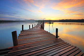 A tranquil wooden jetty stretching into a calm lake at sunrise with colorful sky reflections. HD wallpaper