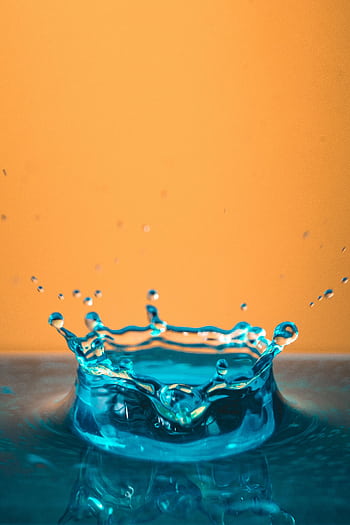 Stunning close-up of a turquoise water splash with a vivid orange background. HD phone wallpaper