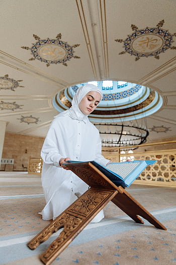 A young woman reading the Quran in a beautifully decorated mosque, symbolizing faith and spirituality. HD phone wallpaper