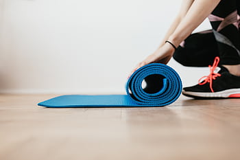 Close-up of a woman preparing for an indoor workout by rolling a blue yoga mat. HD wallpaper