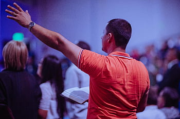 A man worships in a church holding a Bible among a congregation of diverse people. HD wallpaper