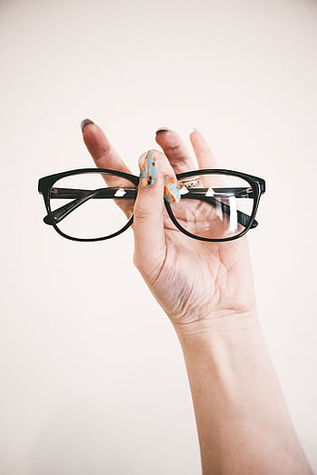 A hand with colorful nail art holding stylish eyeglasses against a light background. HD phone wallpaper