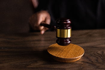 A gavel striking a sound block, symbolizing justice and legal authority in a courtroom setting. HD wallpaper
