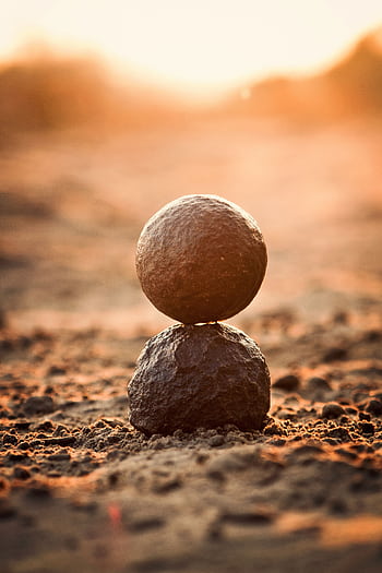 Two stones perfectly balanced on sandy ground at sunset, evoking tranquility and zen. HD phone wallpaper