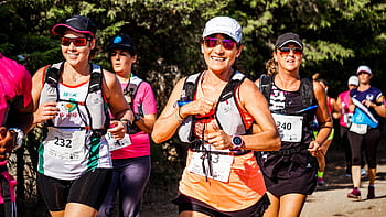 A group of smiling women participating in an outdoor marathon run with race numbers. HD wallpaper