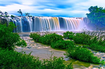 Vibrant waterfall amidst lush greenery under a clear sky, perfect for nature and travel themes. HD wallpaper