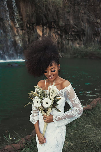 Smiling bride with bridal bouquet by waterfall in elegant white gown. HD phone wallpaper