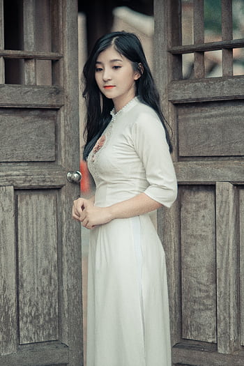 Young woman in elegant white dress standing in a rustic wooden doorway outdoors. HD phone wallpaper
