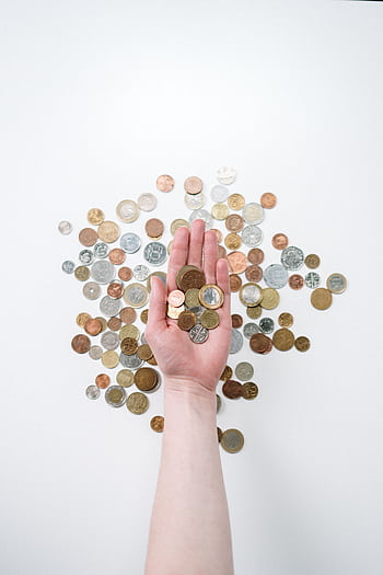 An open hand holds various coins on a white surface, symbolizing finance and currency exchange. HD phone wallpaper