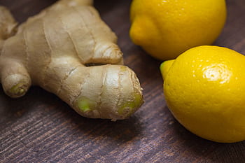 Close-up of fresh ginger root and lemons on a wooden surface showcasing natural ingredients. HD wallpaper