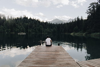 Young man sitting on a wooden pier overlooking a tranquil lake in Flims, Switzerland. HD wallpaper