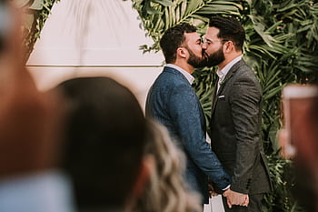 A same-sex couple shares a tender kiss at their wedding ceremony, celebrating love and commitment. HD wallpaper