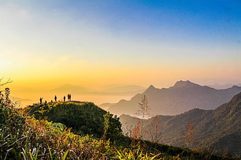 A hiking group enjoys a stunning sunrise view from a mountain peak, surrounded by lush greenery. HD wallpaper