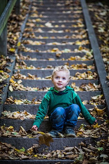 Young boy in green hoodie sitting on outdoor stairs covered with autumn leaves. HD phone wallpaper