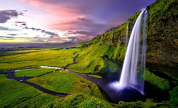 Stunning waterfall cascading over green cliffs during a vibrant Icelandic sunset. HD wallpaper