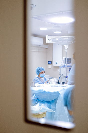 View of a surgeon working in an operating room through a door window, emphasizing medical precision. HD phone wallpaper