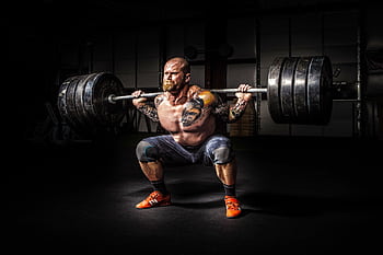 Muscular man lifting heavy weights during an intense squat session inside a gym. HD wallpaper