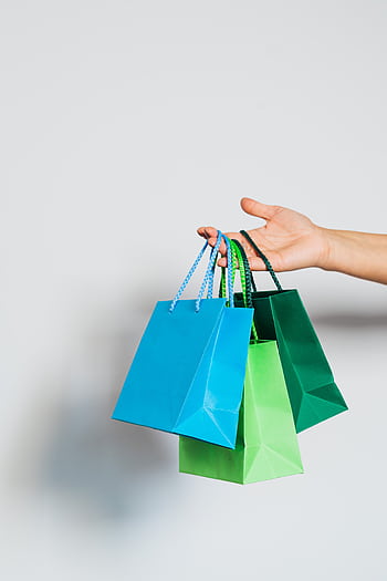 Hand holding three colorful paper shopping bags on a white background. HD phone wallpaper