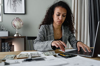 Professional woman analyzing financial documents and counting cash at office desk. HD wallpaper