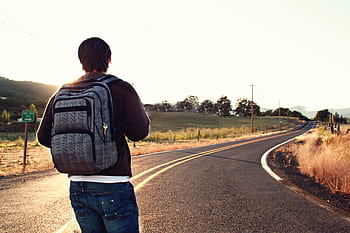 A traveler with a backpack walks on a winding road in the countryside during sunset, symbolizing adventure and dom. HD wallpaper