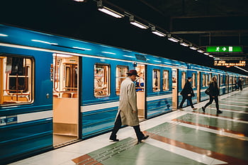 Dynamic scene of passengers moving on a subway platform with a blue train in an urban environment. HD wallpaper
