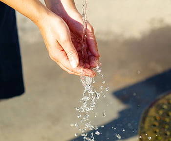 Close-up of hands catching flowing water outdoors, symbolizing freshness and purity. HD wallpaper