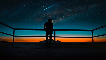 A silhouette of a person observing a vibrant night sky with stars and meteors. HD wallpaper