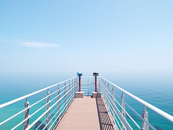 Experience the serenity of a sunny day on a coastal pier overlooking the tranquil sea. HD wallpaper