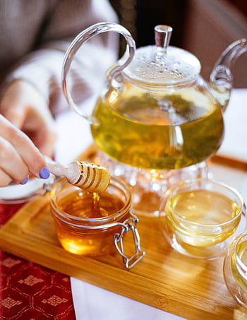 Elegant glass teapot with herbal tea, honey drizzle, and cups on a wooden tray for a perfect tea time setting. HD phone wallpaper