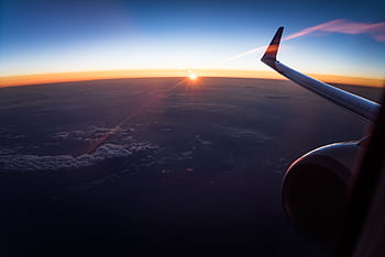 Stunning aerial view from an airplane window showing the wing and a sunset over the clouds. HD wallpaper