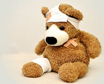 A brown teddy bear with bandages, depicting a playful take on injury recovery in a minimalist setting. HD wallpaper