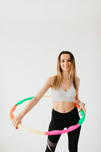 Smiling woman exercises with hula hoop in studio, showcasing fitness and vitality. HD phone wallpaper