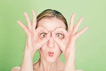 A woman creates a funny face with her hands and eyes against a green background. Perfect for whimsical themes. HD wallpaper
