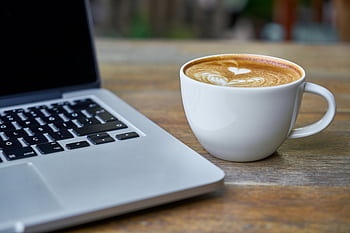 Close-up of a latte coffee with heart art next to a laptop on a rustic wooden table. HD wallpaper