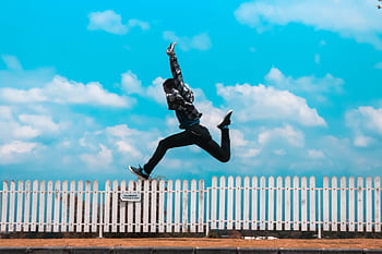 Mid-air capture of a person leaping in front of a picket fence under a bright blue sky. HD wallpaper
