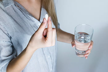 Close-up of a woman holding a pill and a glass of water, ready to take medication. HD wallpaper