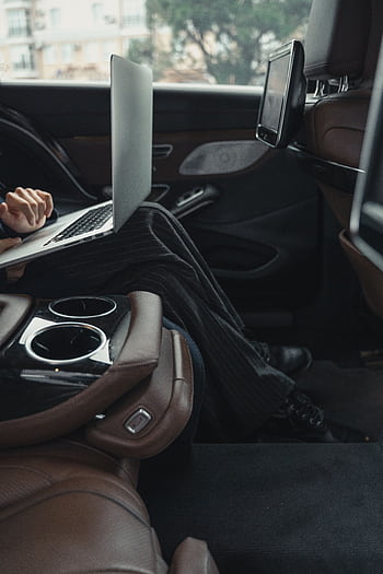 A professional woman working remotely on a laptop inside a luxurious car. Modern executive lifestyle. HD phone wallpaper