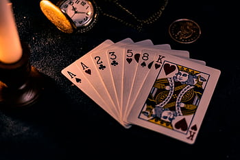 A dimly lit close-up of playing cards with a pocket watch, showcasing a nostalgic casino vibe. HD wallpaper