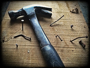 A weathered hammer surrounded by bent nails on a wooden plank, capturing the essence of carpentry work. HD wallpaper