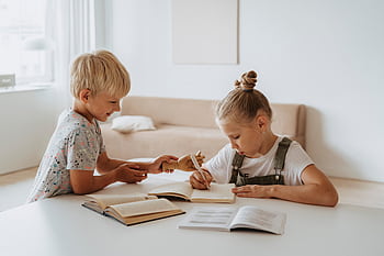 Blonde boy and girl studying together indoors, focusing on writing and learning. HD wallpaper