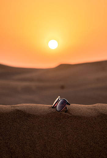 Scenic view of sunglasses on Dubai's desert sand with a stunning sunset backdrop. HD phone wallpaper