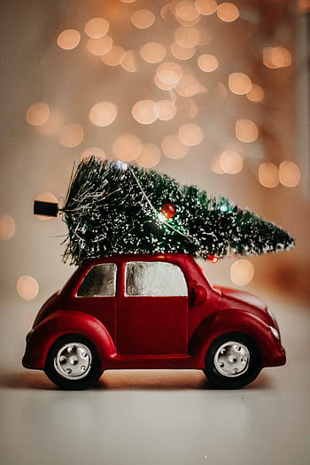 A red toy car carries a Christmas tree, set against a warm bokeh background, celebrating the festive season. HD phone wallpaper