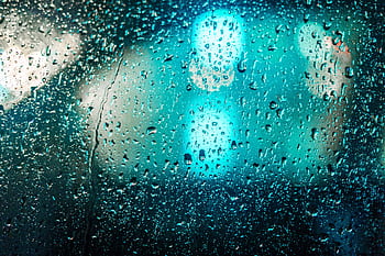 Raindrops on glass with blurred colorful lights creating a moody abstract background. HD wallpaper